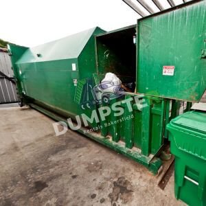 A large green garbage bin positioned in a spacious garage, ready for waste disposal.